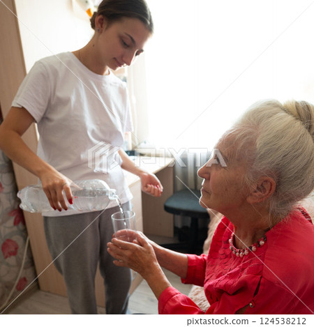 Care and compassion in a cozy room as a young person pours water for an elderly woman reflecting warmth and connection during a quiet moment together Care and compassion in a cozy room as a young person pours water for an elderly woman reflecting warmth and connection during a quiet moment together 124538212