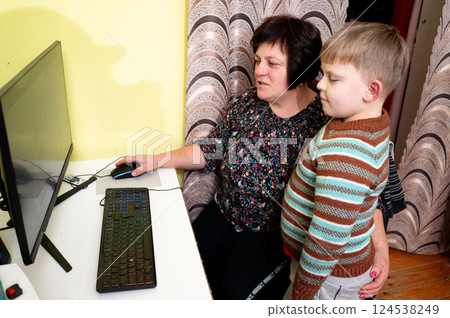 Curious boy watches closely as playful adult navigates the colorful screen in a cozy room filled with warmth and laughter during a quiet afternoon 124538249