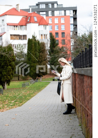 Charming stroll in the city park during autumn, where a fashionable woman enjoys an afternoon break while checking her phone amidst serene surroundings 124538271