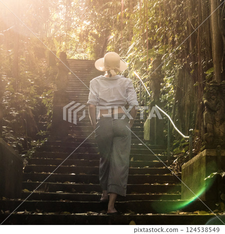Rear view of beautiful fashionable stylish female traveler wearing a hat, walking the staircase of traditional hidu tample around Ubud on Bali. Concept of luxury vacation, exploring and discovering 124538549