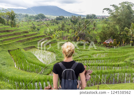 Casual caucasian female tourist wearing small backpack looking at beautiful green rice fields and terraces of Jatiluwih on Bali island, Indonesia. 124538562