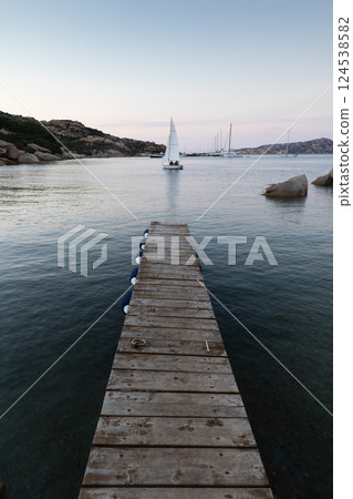Wooden pier and sailboats sailing in evening calm sea of marvellous Porto Rafael, Costa Smeralda, Sardinia, Italy. Symbol for relaxation, wealth, leisure activity. 124538582