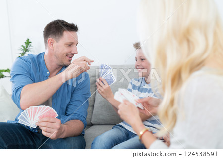 Happy young family playing card game on living room sofa at home. Spending quality leisure time with children and family concept. Cards are generic and debranded. Happy young family playing card game on living room sofa at home. Spending quality leisure time with children and family concept. Cards are generic and debranded. 124538591