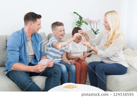 Happy young family playing card game on living room sofa at home. Spending quality leisure time with children and family concept. Cards are generic and debranded. 124538593