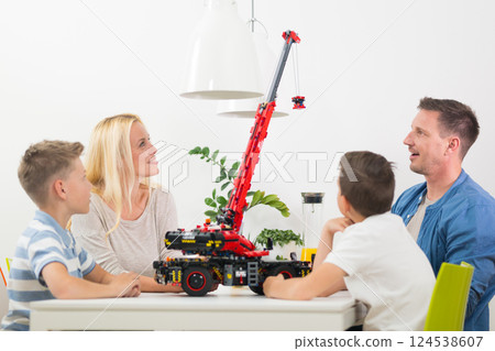 Happy young family playing with toys at dining table at bright modern home. Spending quality leisure time with children and family concept. Happy young family playing with toys at dining table at bright modern home. Spending quality leisure time with children and family concept. 124538607