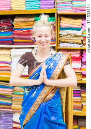 Travel photo of beautiful blond Caucasian tourist woman trying to wear a traditional Indian saree in local saree shop as part of authentic travel experience 124538664