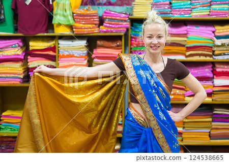 Travel photo of beautiful blond Caucasian tourist woman trying to wear a traditional Indian saree in local saree shop as part of authentic travel experience Travel photo of beautiful blond Caucasian tourist woman trying to wear a traditional Indian saree in local saree shop as part of authentic travel experience 124538665