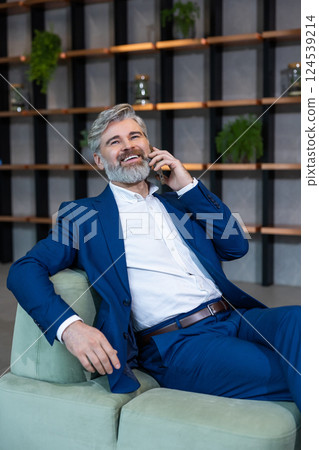 Good-looking well-dressed bearded man sitting in the chair and talking on the phone Good-looking well-dressed bearded man sitting in the chair and talking on the phone 124539214