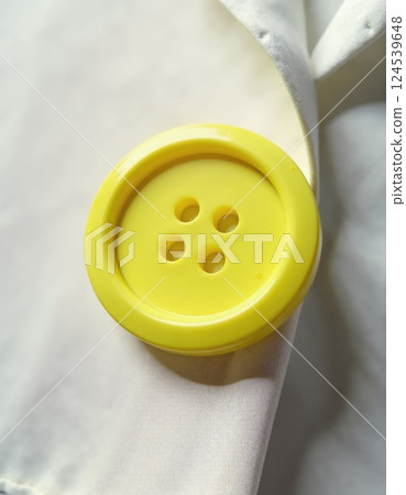 Close-up of a bright yellow button on white fabric for sewing and craft projects 124539648