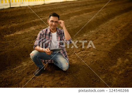 Agronomist holding a laptop and checking soil quality in an agricultural 124540266