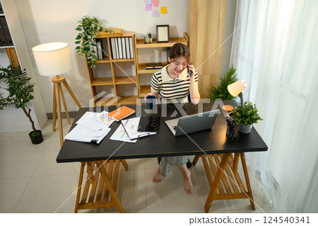 Cheerful young entrepreneur having phone conversation sitting at her workplace 124540341