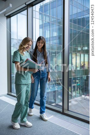 Female doctor in hospital clinic wearing medical uniform reviewing papers with patient 124540473