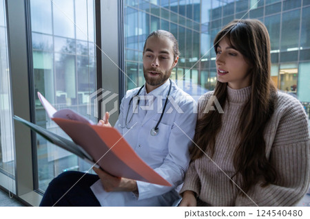 Male doctor in hospital clinic wearing medical uniform reviewing papers with patient 124540480