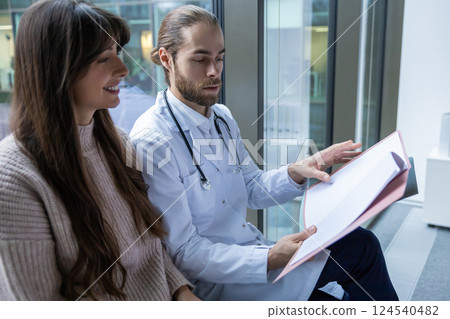 Male diagnostician in clinic talking with patient checking documents in hall Male diagnostician in clinic talking with patient checking documents in hall 124540482