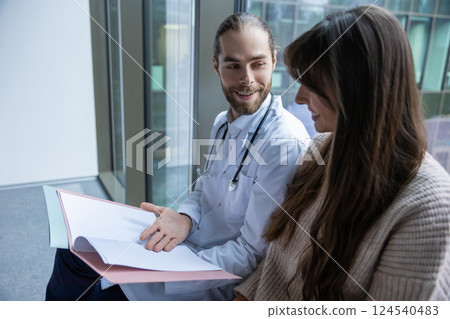 Male specialist holding file and documents discussing treatment with woman patient 124540483