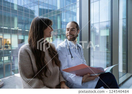 Male doctor in hospital clinic wearing medical uniform reviewing papers with patient Male doctor in hospital clinic wearing medical uniform reviewing papers with patient 124540484