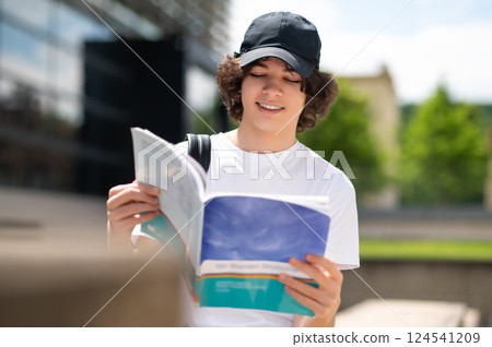 Young university student wearing backpack walking on campus and reading book Young university student wearing backpack walking on campus and reading book 124541209