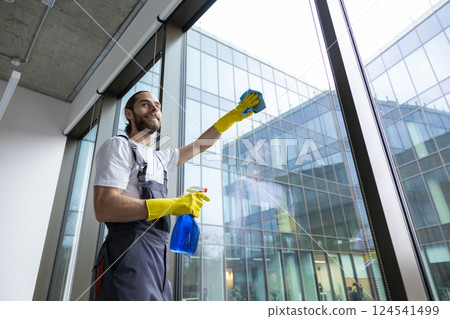 Young service man cleaning windows in the office and looking busy 124541499