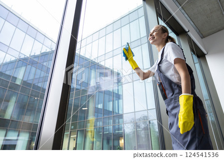 Blonde young woman cleaning the windows and looking involved Blonde young woman cleaning the windows and looking involved 124541536