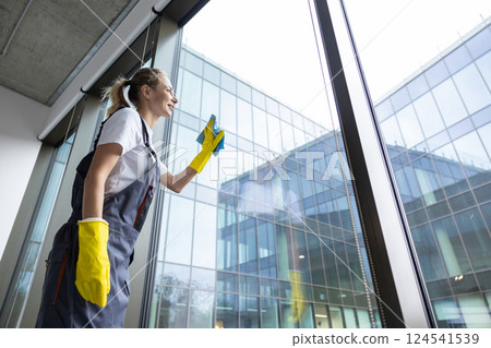 Blonde young woman cleaning the windows and looking involved 124541539