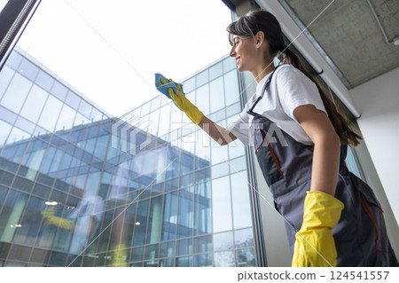 Dark-haired young woman cleaning windows i the office premises 124541557