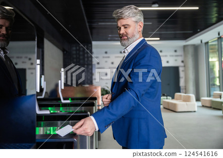 Gray-haired mature business man in dark-blue suit entering office with an access card Gray-haired mature business man in dark-blue suit entering office with an access card 124541616