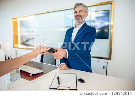 Businessperson handing keys to client after closing successful deal on car in showroom 124542014