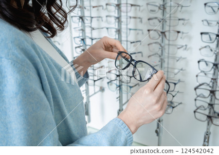 Female customer choosing new glasses in optic shop and looking enjoyed 124542042