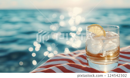 Refreshing highball glass of sparkling water with ice and lemon by the pool on a sunny day, with waves glimmering in the background 124542302