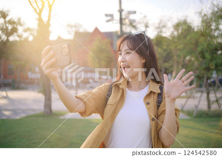 Traveler asian woman in her 30s making a livestream or selfie with a smartphone in evening scene while solo travel in Bangkok, Thailand. 124542580