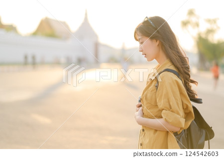 Traveler asian woman in her 30s stands bathed in the golden glow of sunset, embracing the freedom of exploration. on summer holiday weekend vacation trip in Bangkok, Thailand Traveler asian woman in her 30s stands bathed in the golden glow of sunset, embracing the freedom of exploration. on summer holiday weekend vacation trip in Bangkok, Thailand 124542603