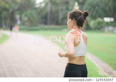 Shoulder pain problem. woman jogger. 30s asian female wearing white sportswear holding her shoulder with pain after running exercise in public park. Shoulder pain problem. woman jogger. 30s asian female wearing white sportswear holding her shoulder with pain after running exercise in public park. 124542647