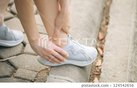 Sprained ankle problem. woman jogger. 30s asian female wearing sportswear holding her ankle with pain after running exercise in public park. Sprained ankle problem. woman jogger. 30s asian female wearing sportswear holding her ankle with pain after running exercise in public park. 124542656