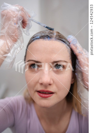 Caucasian woman carefully applying hair dye, looking down 124542933