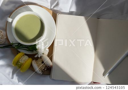 White pages of notebook copy space Sweet yellow macaron dessert Cup of green plant based matcha tea latte in cozy morning bed atmosphere. Creative holiday romantic date idea. Herbal prebiotic fiber 124543105
