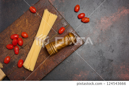 Uncooked spaghetti pasta tied with twine, cherry tomatoes, and a wooden pepper grinder on a rustic wooden cutting board Uncooked spaghetti pasta tied with twine, cherry tomatoes, and a wooden pepper grinder on a rustic wooden cutting board 124543666