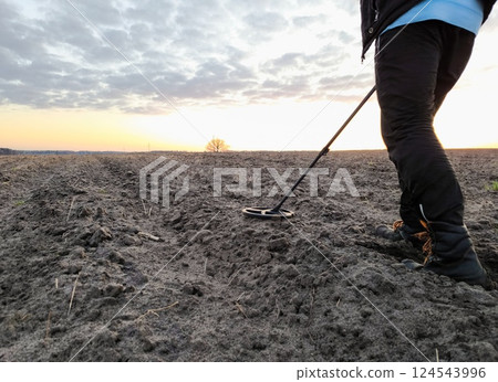 Man with a metal detector in a field in the evening. Metal detecting field. Copy space 124543996
