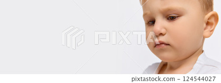 Close-up portrait of serious toddler boy in white shirt with thoughtful expression against white background. 124544027