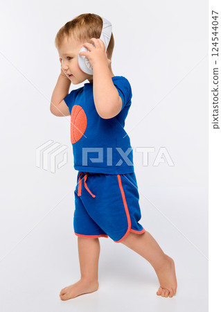 Boy walking in headphones, smiling, listening to music against white studio background. 124544047