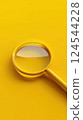 Close-up of a golden magnifying glass on a yellow surface 124544228