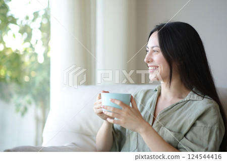 Happy asian woman drinking and looking through a window 124544416