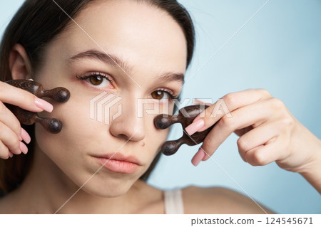 Young woman practicing facial massage with wooden tools in a light setting 124545671