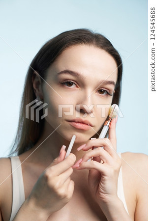 Woman applying makeup with brushes against a light blue background Woman applying makeup with brushes against a light blue background 124545688