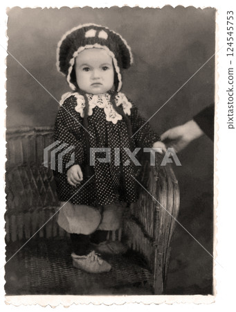Vintage portrait of a cute little girl standing in a chair. The mother's hand is holding the girl. Retro photo from 1946. Vintage portrait of a cute little girl standing in a chair. The mother's hand is holding the girl. Retro photo from 1946. 124545753
