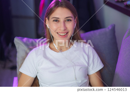Wearing headphones and plaid shirt in a white T-shirt, young woman 20s sitting at desk with laptop 124546013