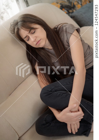 Young woman post-traumatic stress disorder experiencing headache while sitting depression on a couch in a modern living room home during daytime suffers from a psychological disorder, syndrome Young woman post-traumatic stress disorder experiencing headache while sitting depression on a couch in a modern living room home during daytime suffers from a psychological disorder, syndrome 124547293