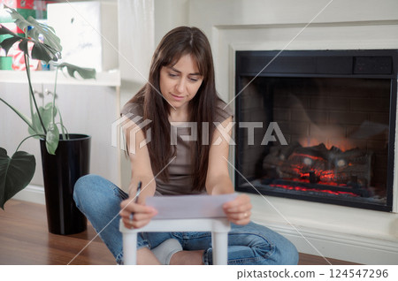 Young lady is seated at a kitchen table, attentively using a pen to write on a piece of paper writes a letter Young lady is seated at a kitchen table, attentively using a pen to write on a piece of paper writes a letter 124547296