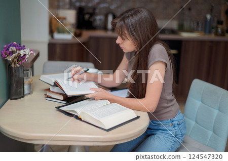 Woman student learning and preparing exam at home. Woman reading textbook and taking notes 124547320