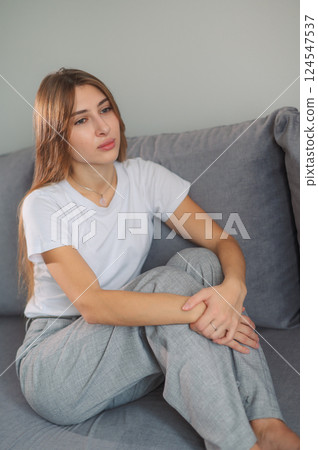 Young woman post-traumatic stress disorder experiencing headache while sitting depression on a couch in a modern living room home during daytime vertical photo 124547537