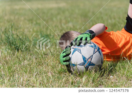 Close-up of goalkeeper boy holding soccer ball on grass. 124547576